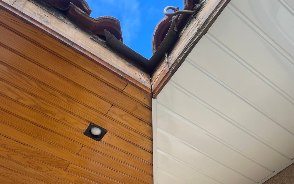 Angle de débord de toiture avec sous-face en lambris bois d'origine à gauche et habillage PVC blanc neuf à droite