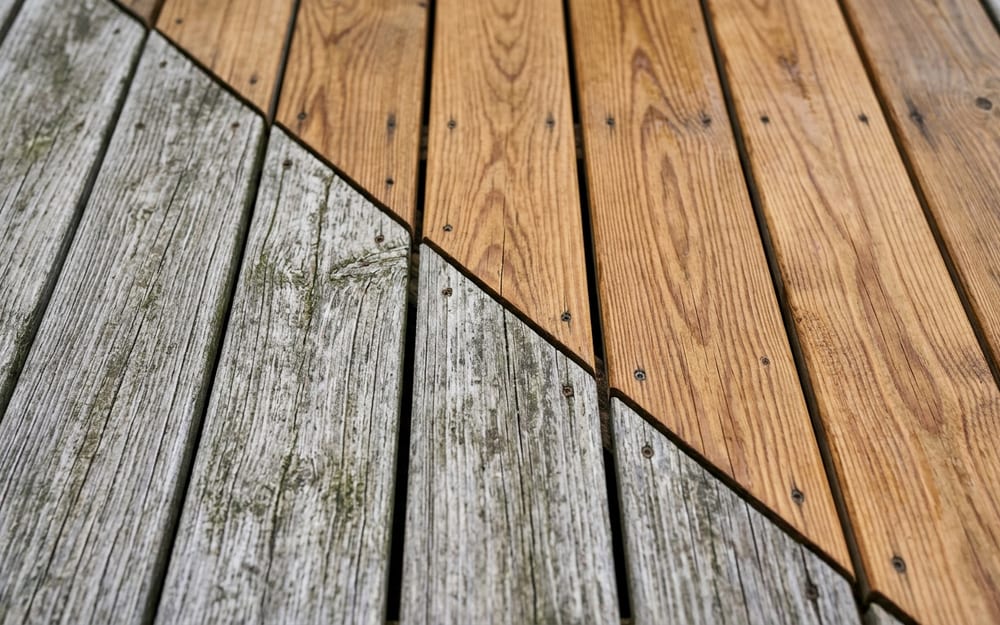 Terrasse en bois dont une moitié est encore grise et fibreuse et l'autre dégrisée, retrouvant sa teinte miel